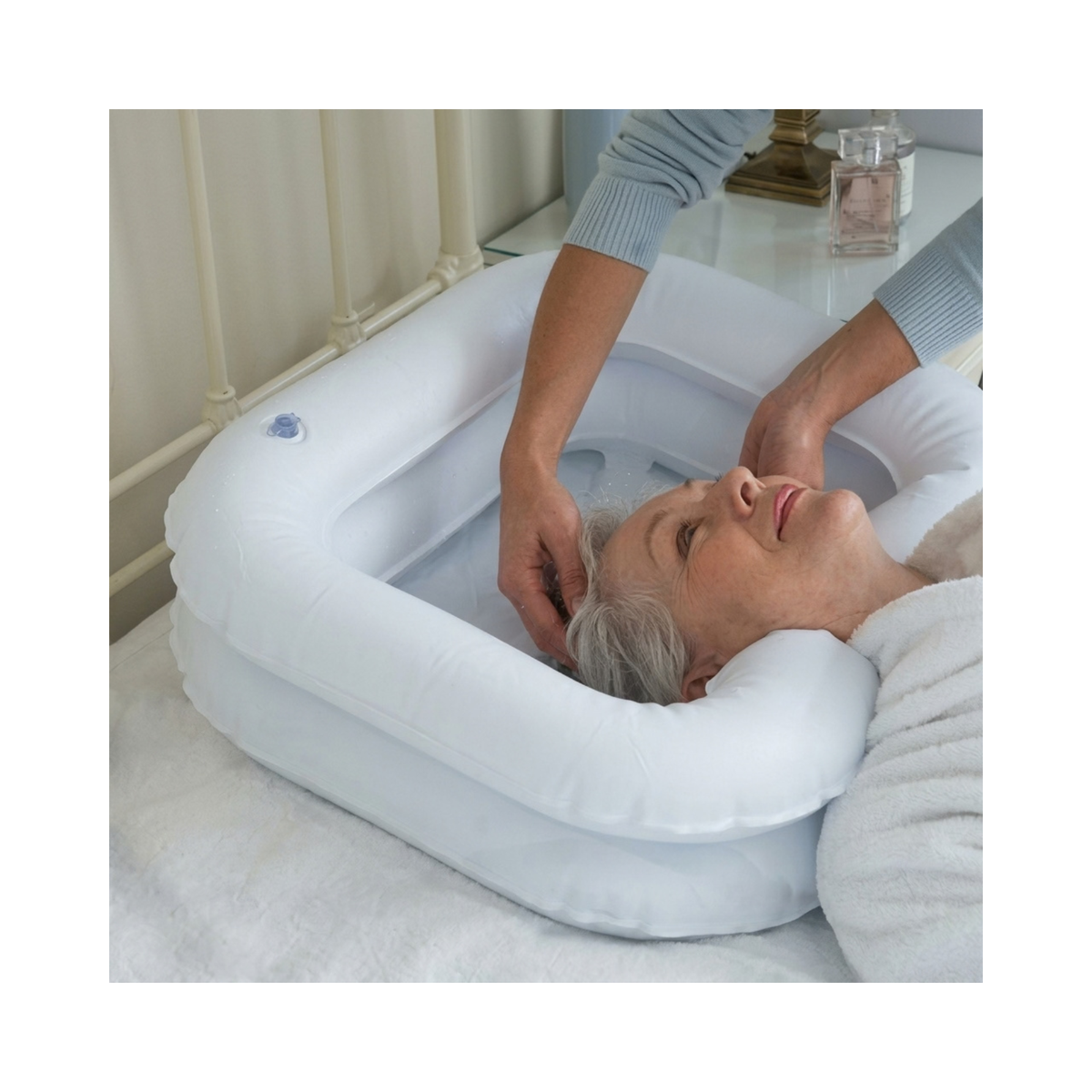Mujer recostada en la cama mientras le lavan el pelo en un lavapelo inflable